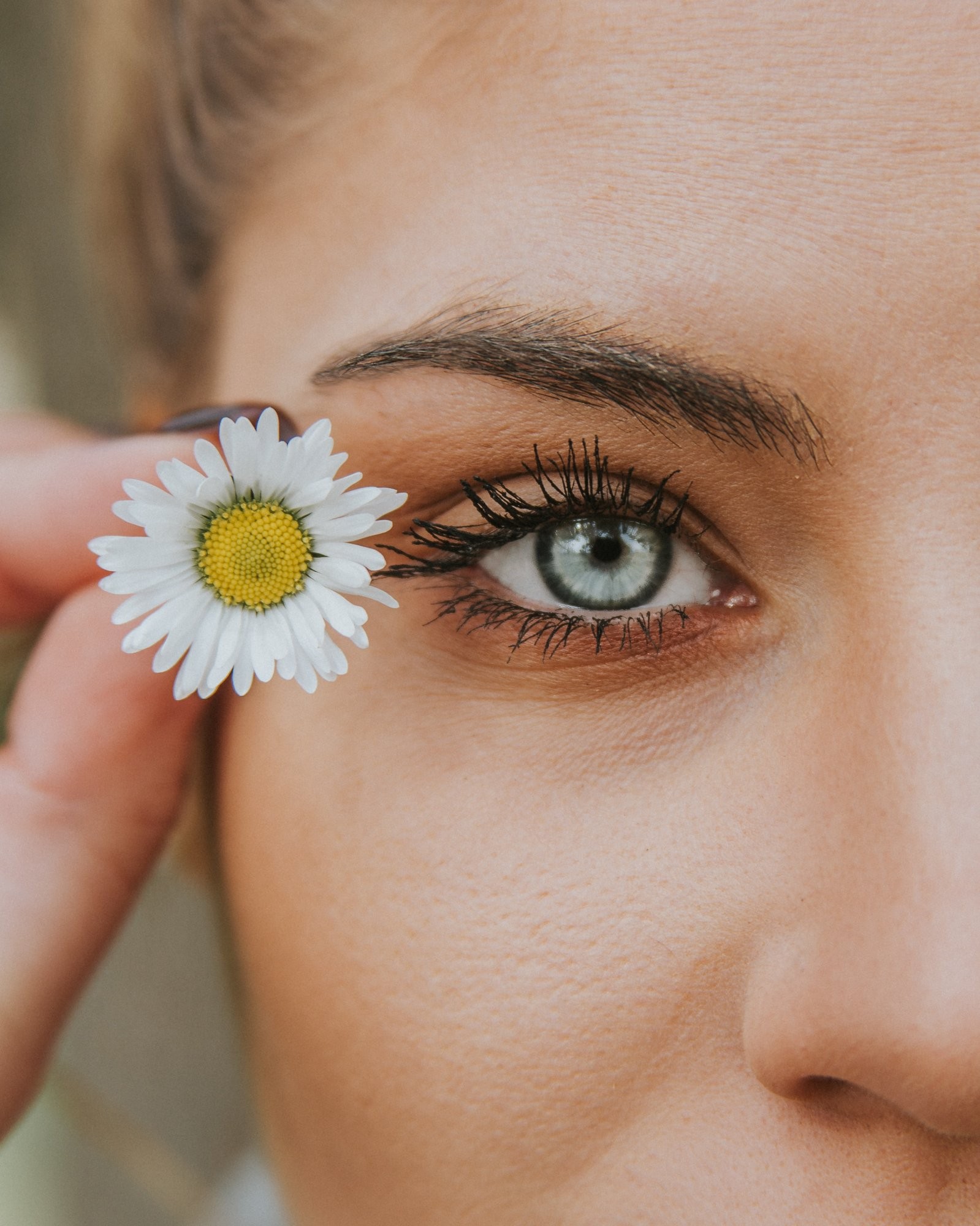 A daisy held beside a bright eye and healthy skin